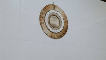 Une pièce avec un mur recouvert de carreaux blancs, une tapisserie murale tissée et une échelle en bambou.