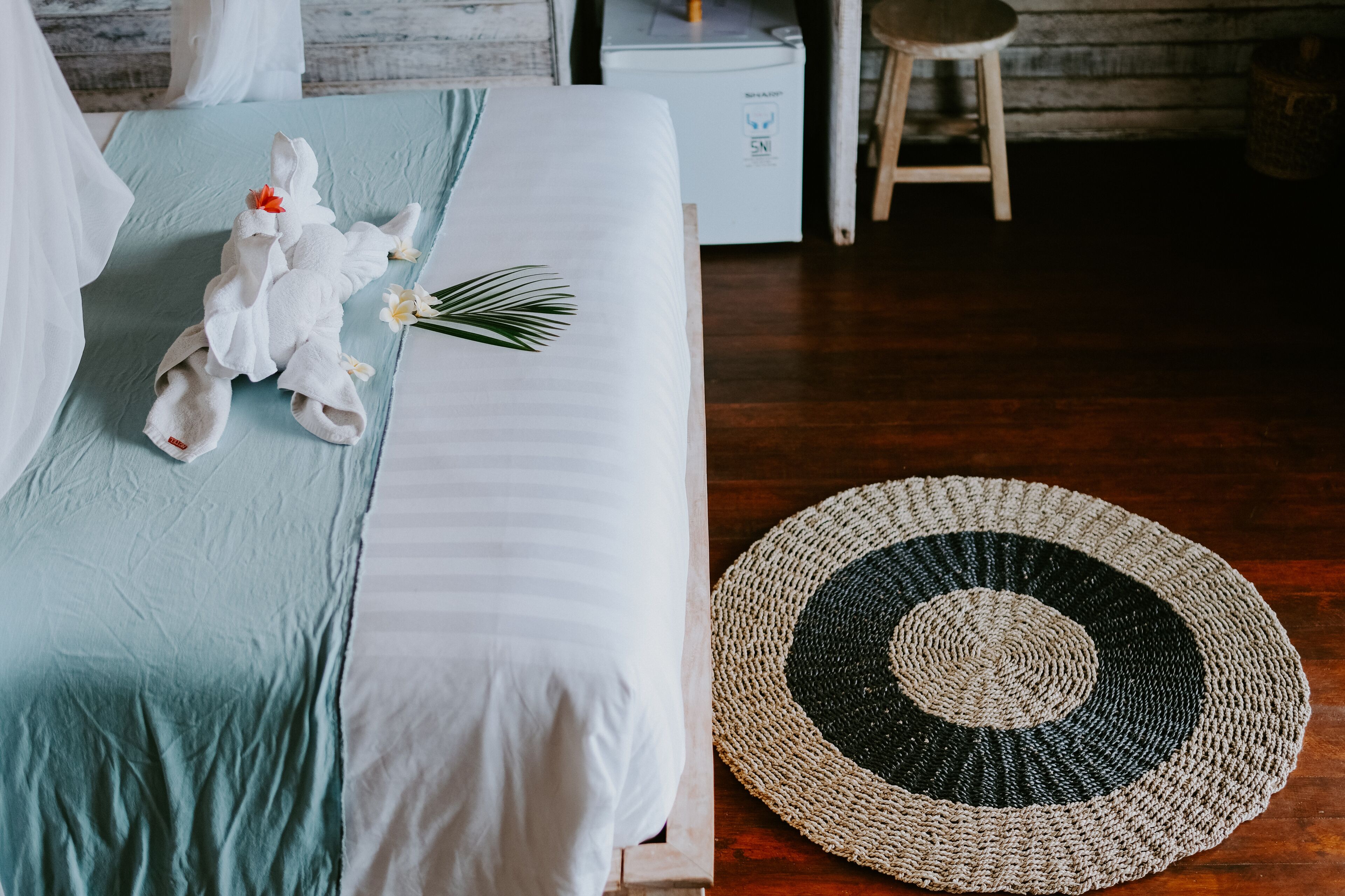 A neatly made bed with a teal and white bedspread, a crocheted doily, and a small bouquet of flowers.