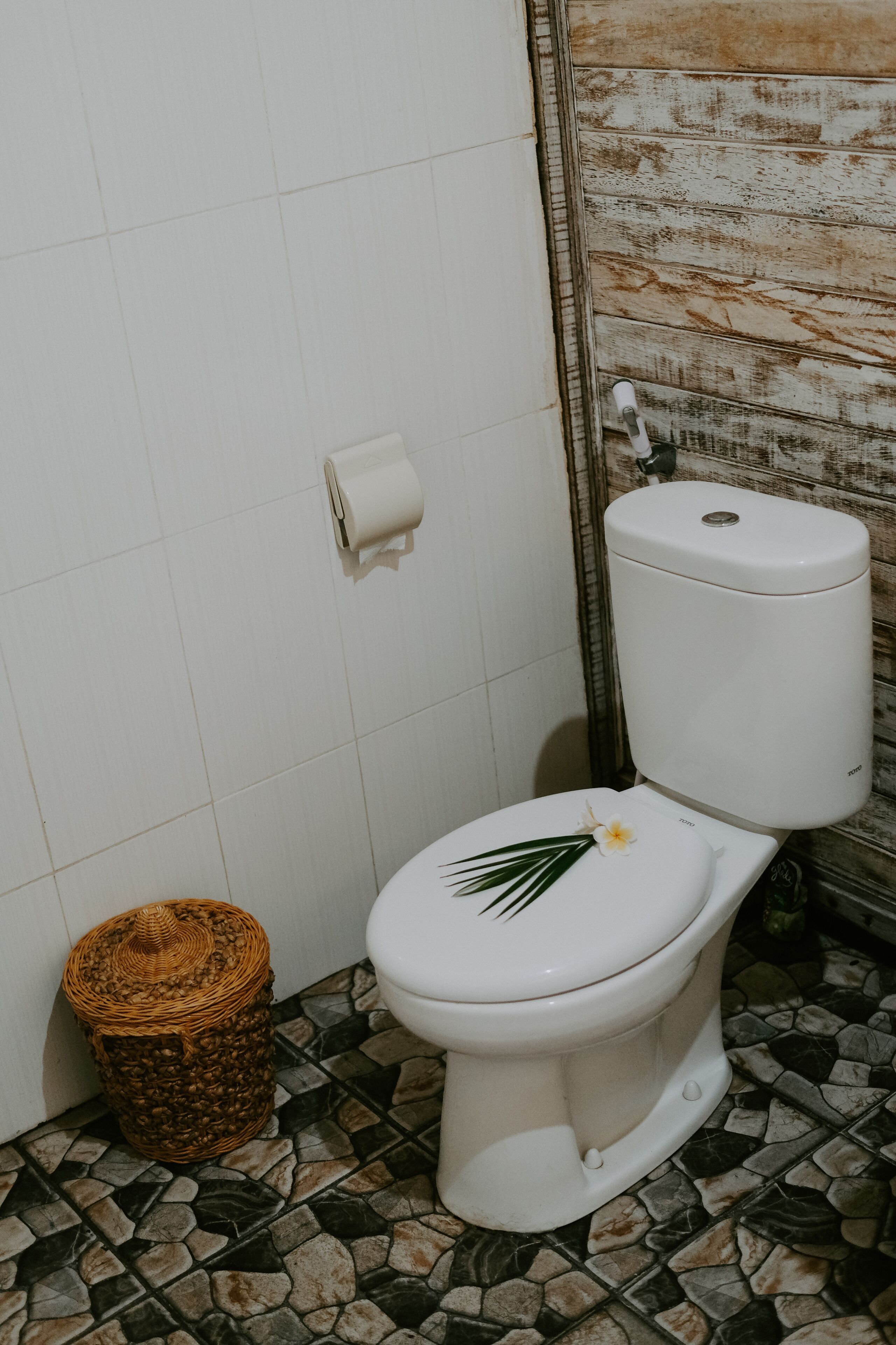 A bathroom with a white toilet, a roll of toilet paper, a wicker basket, and a mosaic tile floor.