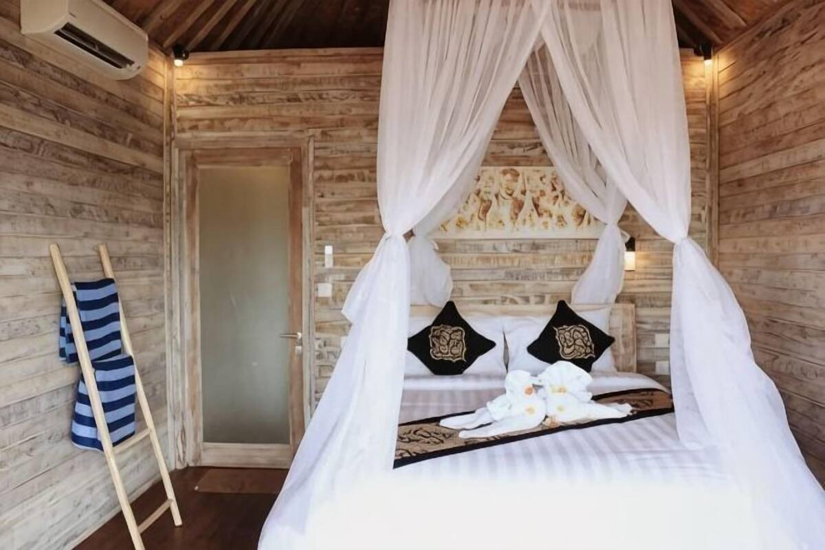 Een houten kamer in blokhutstijl met een bed onder een hemelbed, een ladder en een deur.