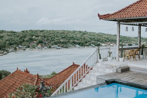 Área da piscina com vista para um corpo d'água e uma colina ao fundo.