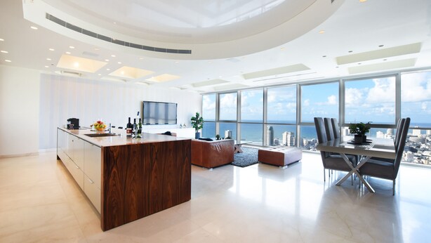 A modern kitchen with a central island, a dining area with a view of the city, and a large window overlooking the ocean. - Tower Sea View Luxury 32 Floor Apartment (Tel Aviv)
