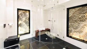A modern bathroom with a glass-enclosed shower, a bench, and two large framed artworks on the walls. - Tower Sea View Luxury 32 Floor Apartment (Tel Aviv)