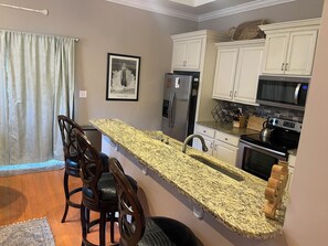A kitchen with granite countertops, white cabinets, a refrigerator, a microwave, and a kettle. - Crabshack in the Promised Land (Morehead City)