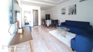 A modern living room with a flat-screen TV, a blue sofa, a dining table with chairs, and a kitchen area in the background. - Chinita Boutique Hotel (Dauis)