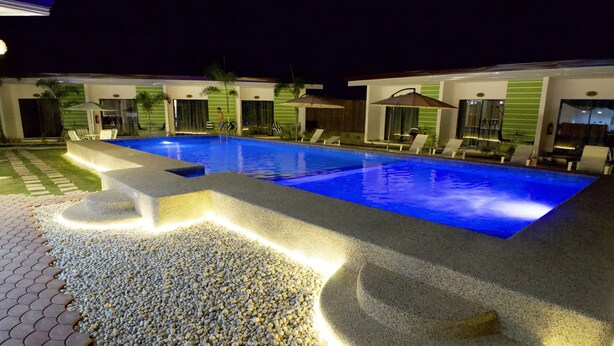 A swimming pool with lounge chairs and umbrellas, surrounded by a pebble walkway. - Chinita Boutique Hotel (Dauis)