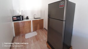 A compact kitchen with a stainless steel refrigerator, wooden cabinets, a sink, and a microwave. - Chinita Boutique Hotel (Dauis)