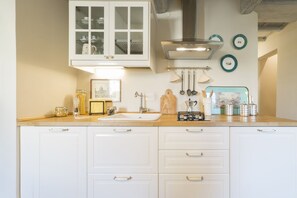 Una cocina con armarios blancos, un lavamanos doble y una campana extractora. Hay platos decorativos en la pared y una foto enmarcada sobre el lavamanos.