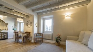 A room with a wooden floor, a dining table with chairs, a sofa, a radiator, and wall-mounted clocks. - A delightful apartment for 5 people in the heart of San Frediano and close to Piazza S. Spirito (FIrenze)