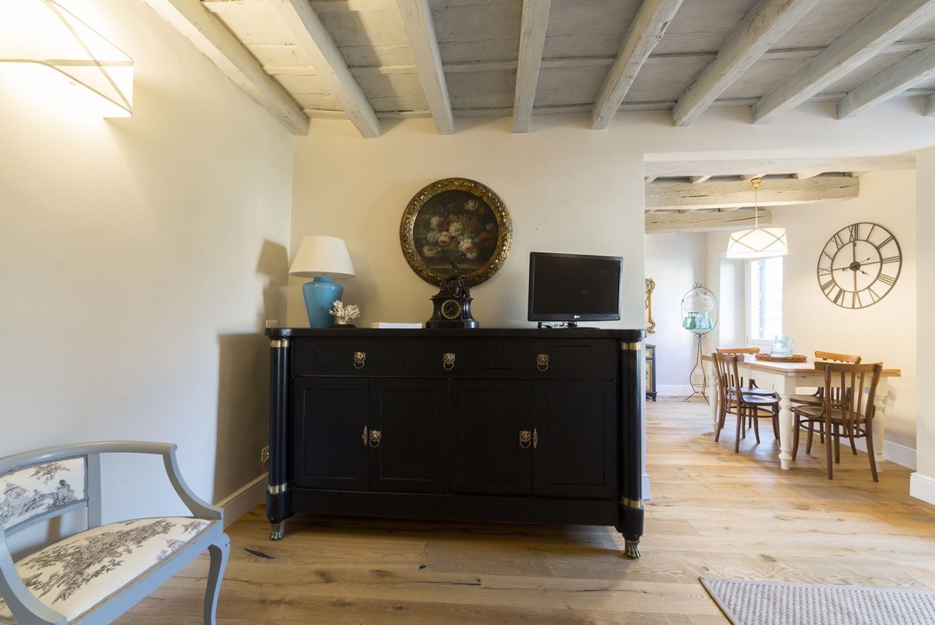 Una habitación con un armario de madera oscura, un televisor, un reloj y una zona de comedor con sillas y una mesa.