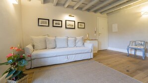 A room with a white sofa, a wooden floor, a white rug, a wall-mounted light, and a framed picture. - A delightful apartment for 5 people in the heart of San Frediano and close to Piazza S. Spirito (FIrenze)
