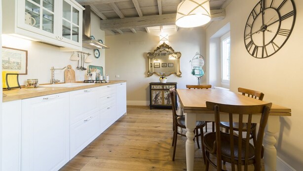 A kitchen with white cabinets, a wooden dining table, and a large wall clock. - A delightful apartment for 5 people in the heart of San Frediano and close to Piazza S. Spirito (FIrenze)