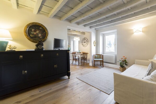 A room with a dark wooden cabinet, a television, a dining area with chairs and a table, and a window with a view.