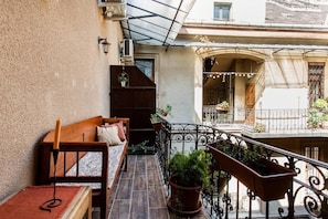 Relax on the balcony with a comfortable bench and table, surrounded by lush potted plants.