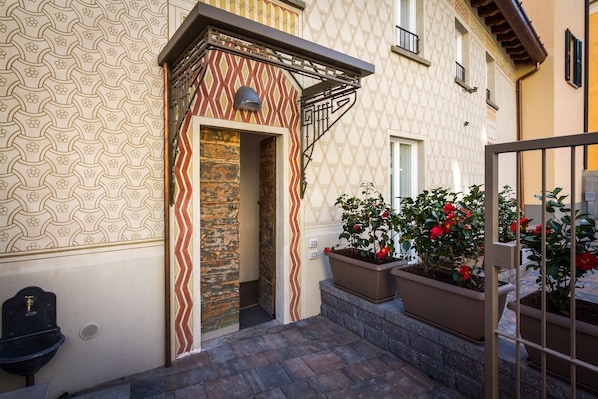 A narrow outdoor corridor with patterned walls, a stone pillar, and potted plants with red flowers. - Perlasca house UP Cernobbio (Cernobbio)