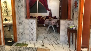 Una stanza con pavimento in marmo, un tavolo da pranzo con tovaglia fantasia, una finestra con tende rosse e un armadio in legno.