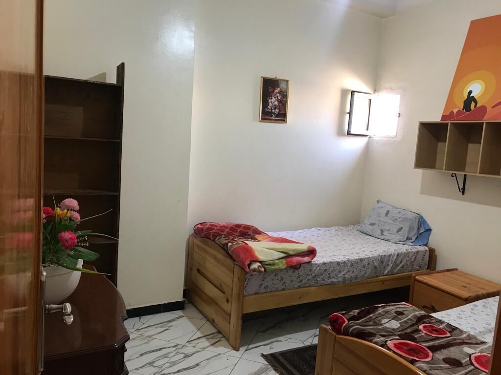Ein kleines, gemütliches Schlafzimmer mit einem Einzelbett, einem Nachttisch, einem Holzschrank und einem an der Wand befestigten Regal.