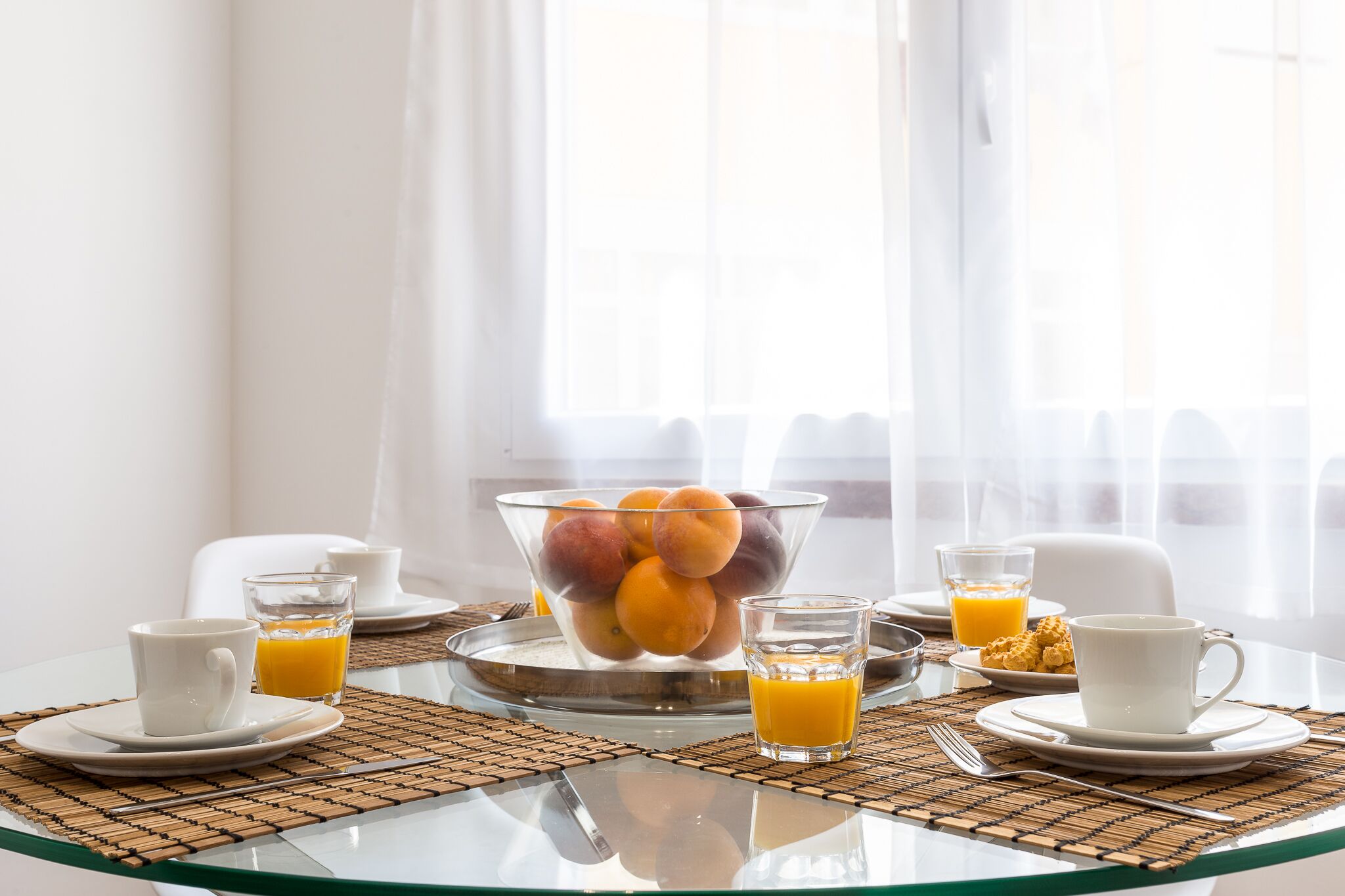 A breakfast table with a fruit bowl, orange juice, and coffee cups.