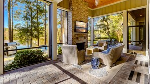 A spacious outdoor area with a stone fireplace, wicker furniture, and large windows overlooking a lake. - 85 Mooring Buoy -Dock, Private Pool & Lagoon Views. 176 Yards to the ocean (Hilton Head Island)
