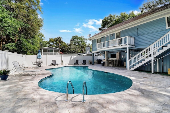 Une piscine à bord incurvé, entourée d’un patio aménagé avec des chaises longues et un espace salon couvert.