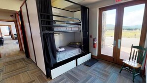 A bunk bed room with a view of the outdoors, an exit sign, and a chair near the door.