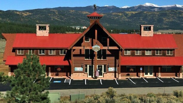 A large, two-story building with a red roof and stone facade, featuring a central entrance and multiple windows.