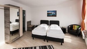 A modern bedroom with two beds, a mirror, a painting, and a chair. - Hotel am Nikolaiort (Osnabrueck)