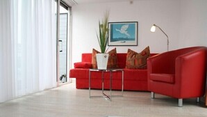 A modern living room with a red sofa, a small table with a plant, and a framed picture on the wall. - Hotel am Nikolaiort (Osnabrueck)