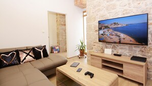 Un salon avec un mur en pierre, une grande télévision, un canapé, une table basse et un meuble pour la télévision.