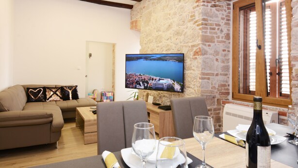 Un salon chaleureux avec un mur en pierre, un téléviseur à écran plat, une table à manger dressée pour deux personnes et un canapé agrémenté de coussins décoratifs.