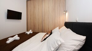 Une chambre d’hôtel moderne, dotée d’une armoire en bois, d’un téléviseur à écran plat et de serviettes soigneusement pliées sur le lit.