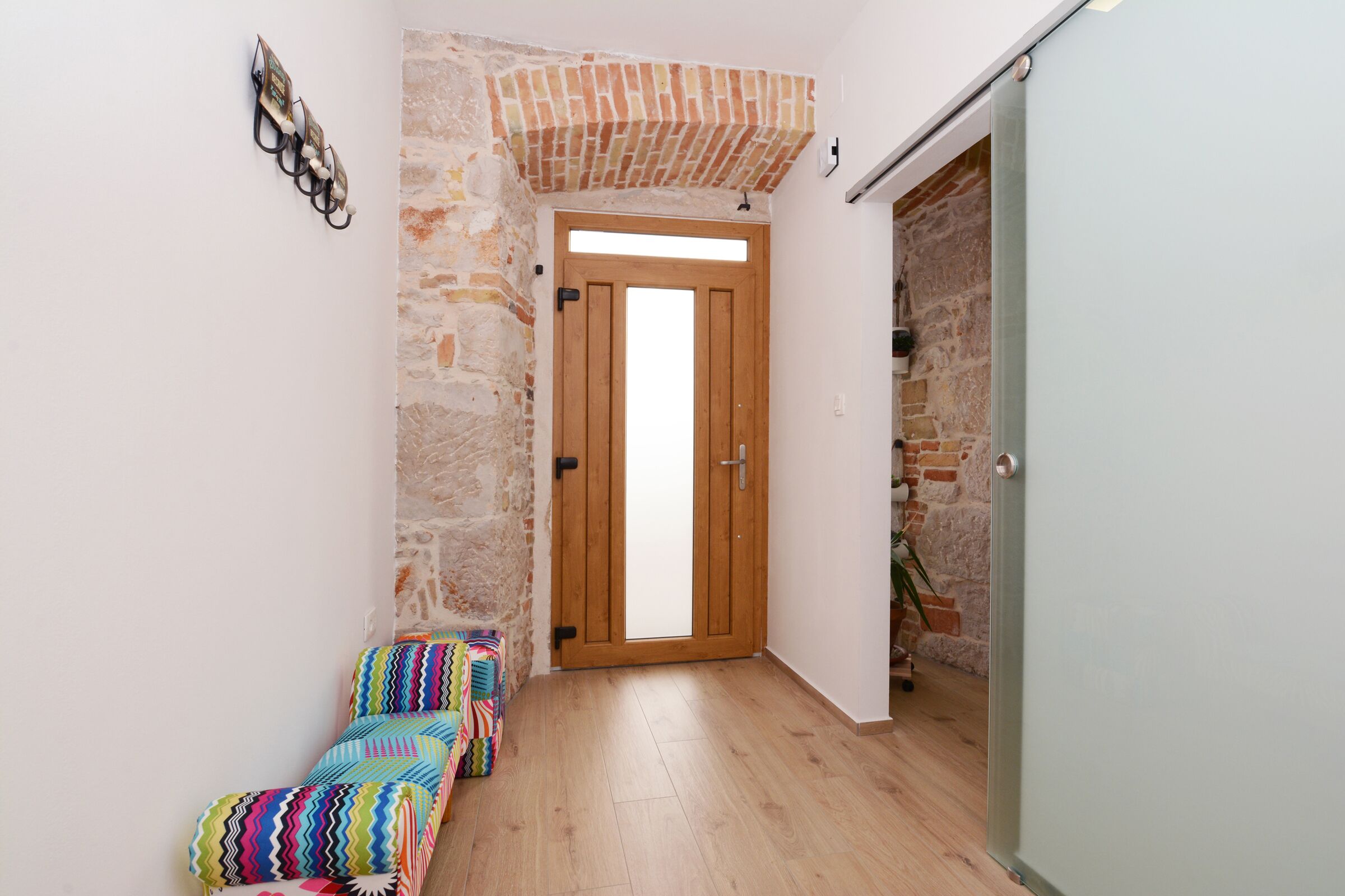 Un pasillo estrecho con una puerta de madera, paredes de piedra y un banco con cojines de colores.