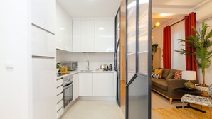 Una cocina compacta con armarios blancos, un microondas y un lavabo. Hay una zona de comedor con un sofá y una mesa, y una planta en maceta.