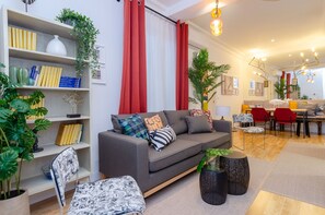 A modern living room with a grey sofa, bookshelves, and a dining area with red chairs.