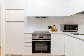 A modern kitchen with white cabinetry, a built-in oven, a microwave, and a stainless steel sink.