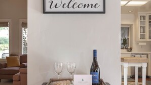 A welcome sign above a tray with two glasses and a bottle of wine, a sign with the Sanctuary logo, and a wooden table in a room with a couch and a kitchen in the background.