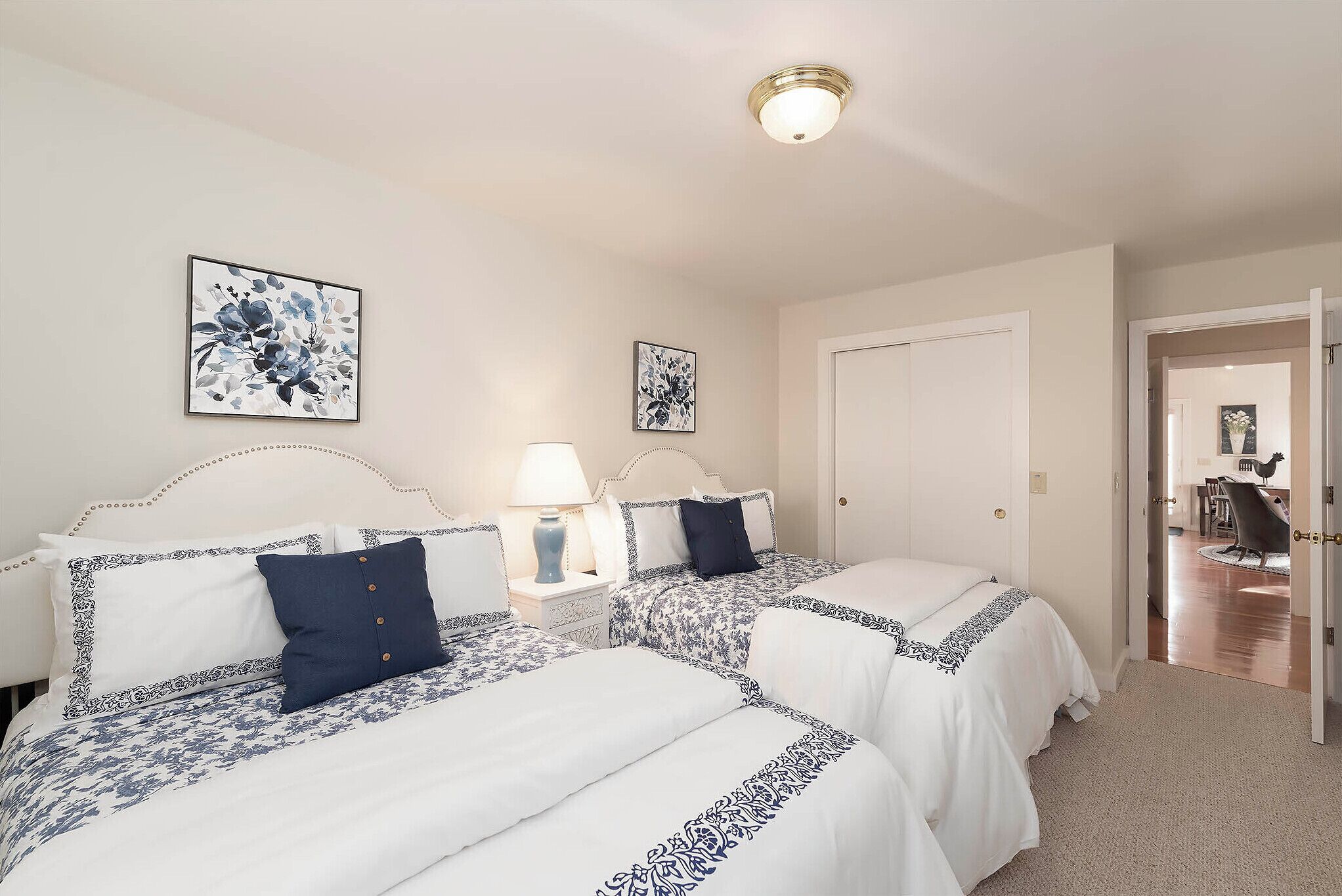 Ett hotellrum med två sängar, var och en med ett vitt och blått mönstrat sängöverkast, ett nattduksbord med en lampa och två inramade blomstermotiv på väggen.