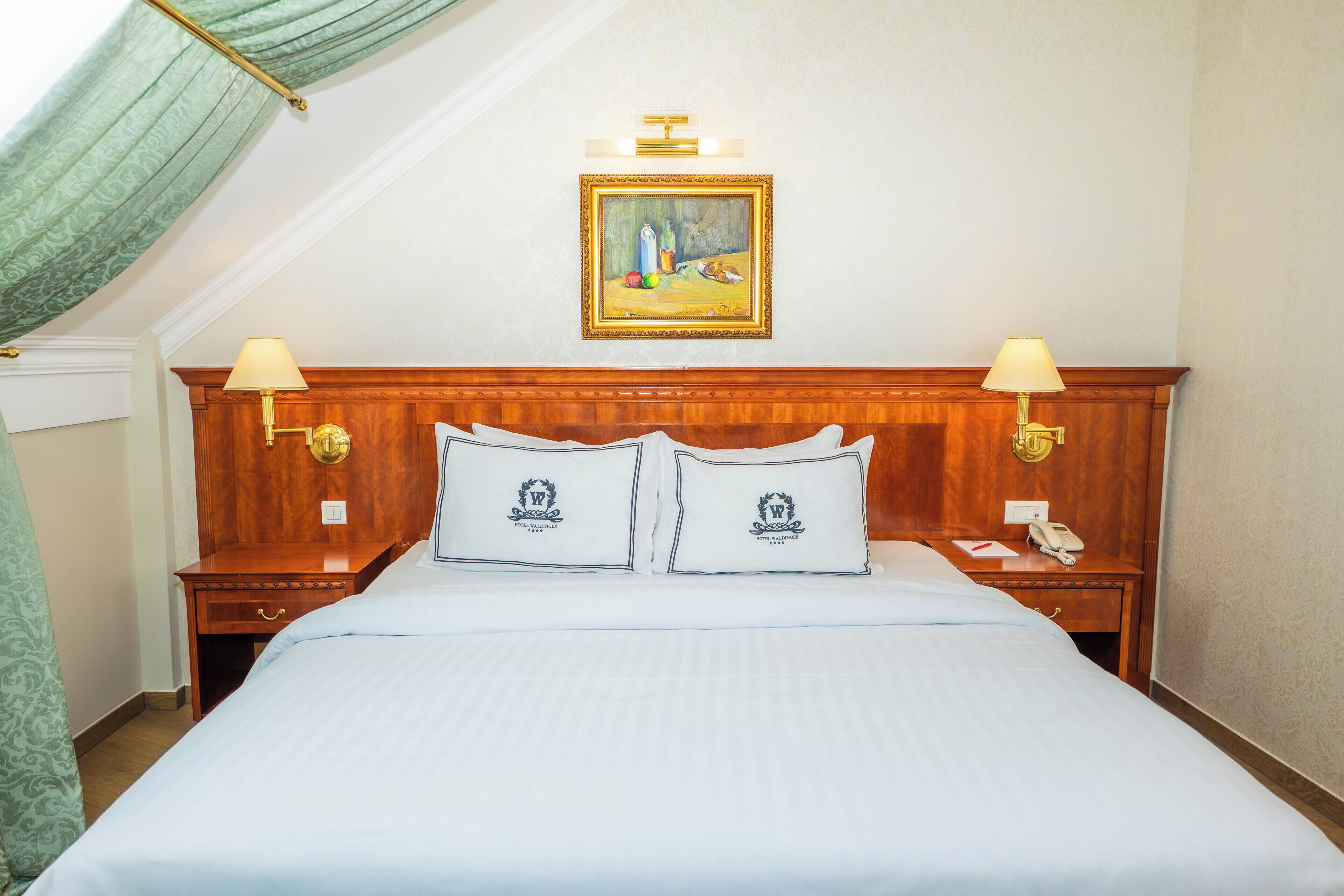 A hotel room with a large bed, two bedside tables with lamps, a painting on the wall, and a wooden headboard.