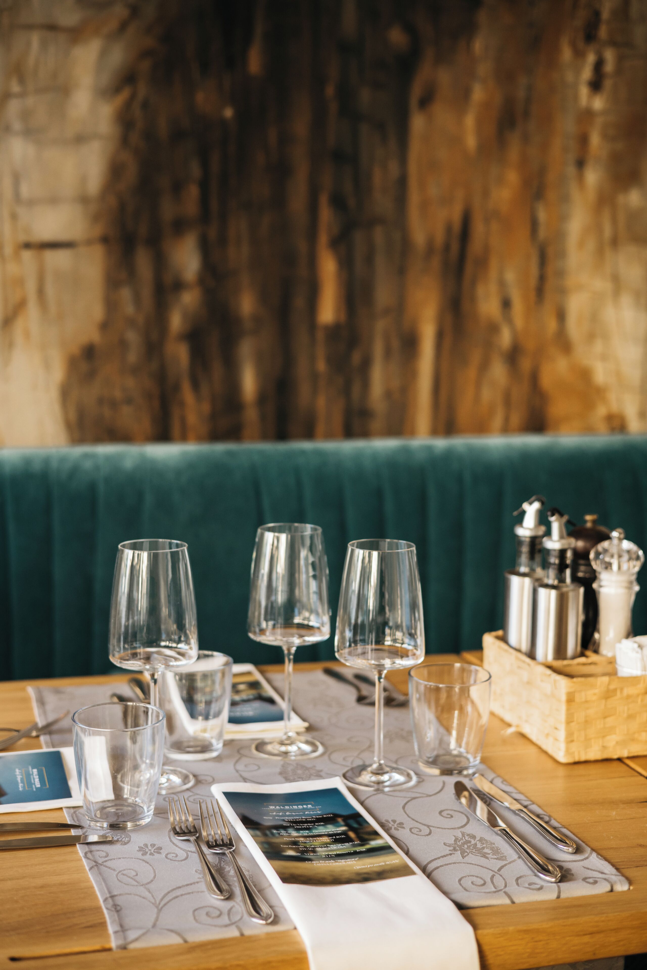 A dining table set with clear glasses, cutlery, and a menu.