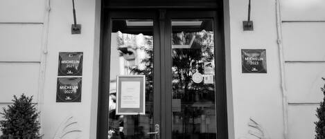 Fotografía en blanco y negro de la entrada de un edificio con un doble acceso, dos macetas y un letrero que dice "WALDINGER LOUNGE BAR, RESTAURANT, WINE BAR".