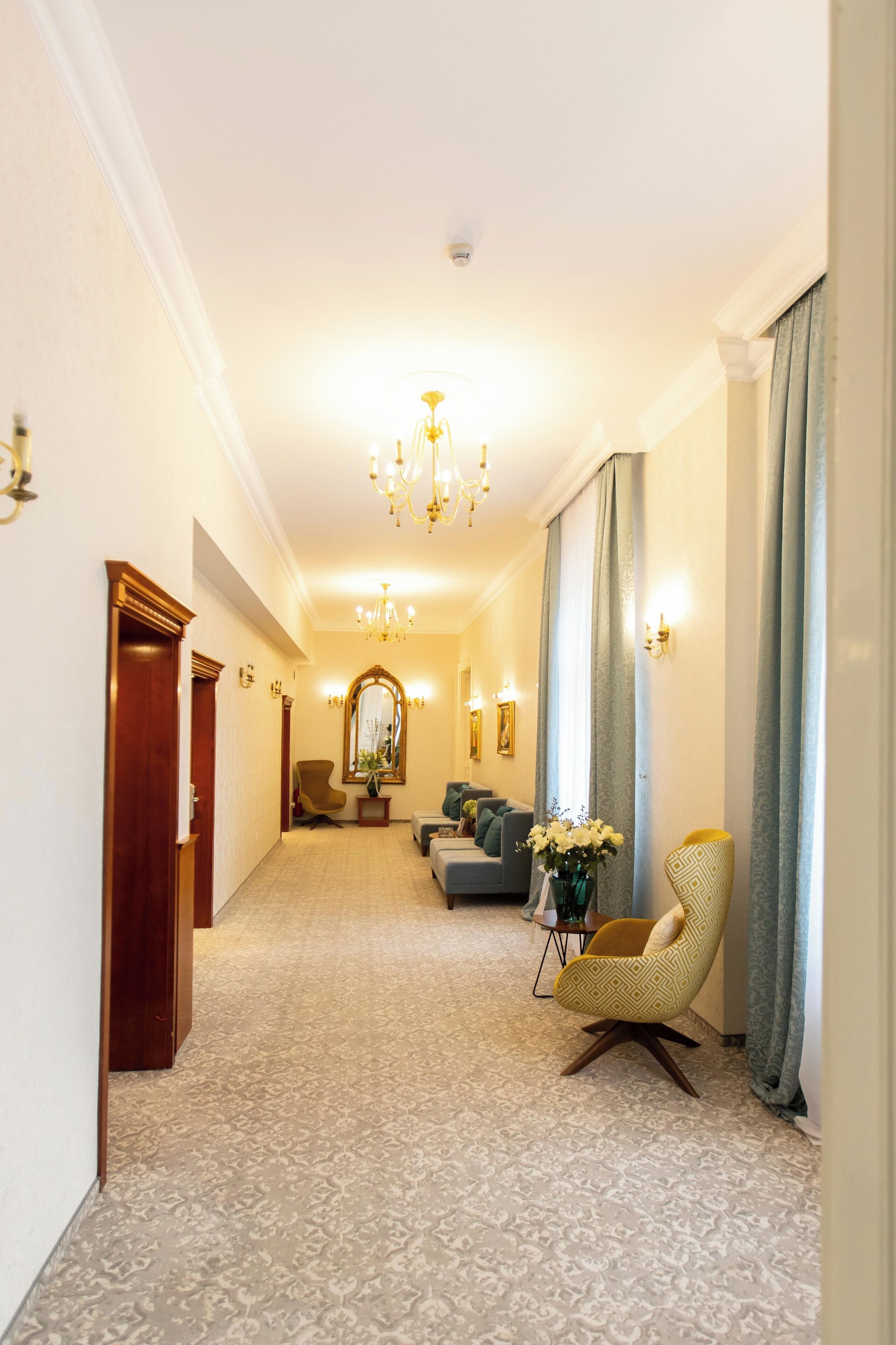 Een hotelgang met een kroonluchter, een bank, een stoel en een spiegel.