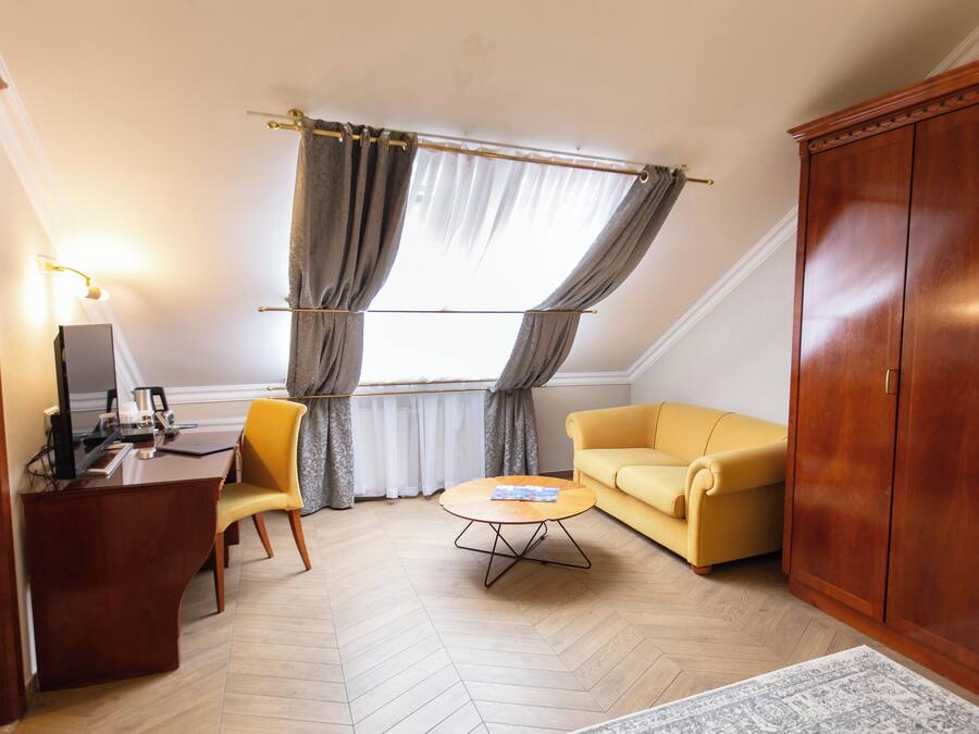 Una habitación con un escritorio de madera, un sofá amarillo, una mesa redonda de centro y un armario.