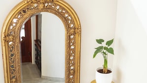 A staircase with a gold-framed mirror, a potted plant on a gold stool, and a wall-mounted light fixture. - Hotel Waldinger (Osijek)