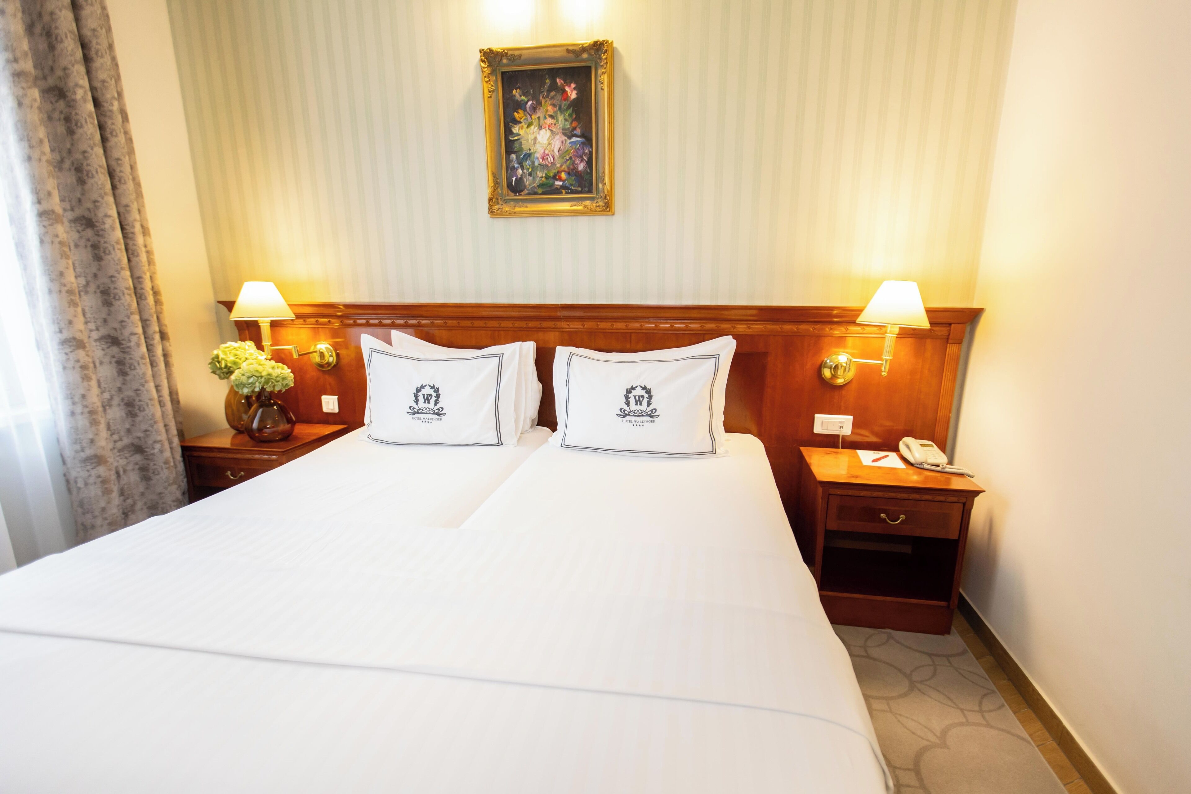 A hotel room with a large bed, two bedside tables with lamps, a nightstand with a phone, and a framed picture on the wall.