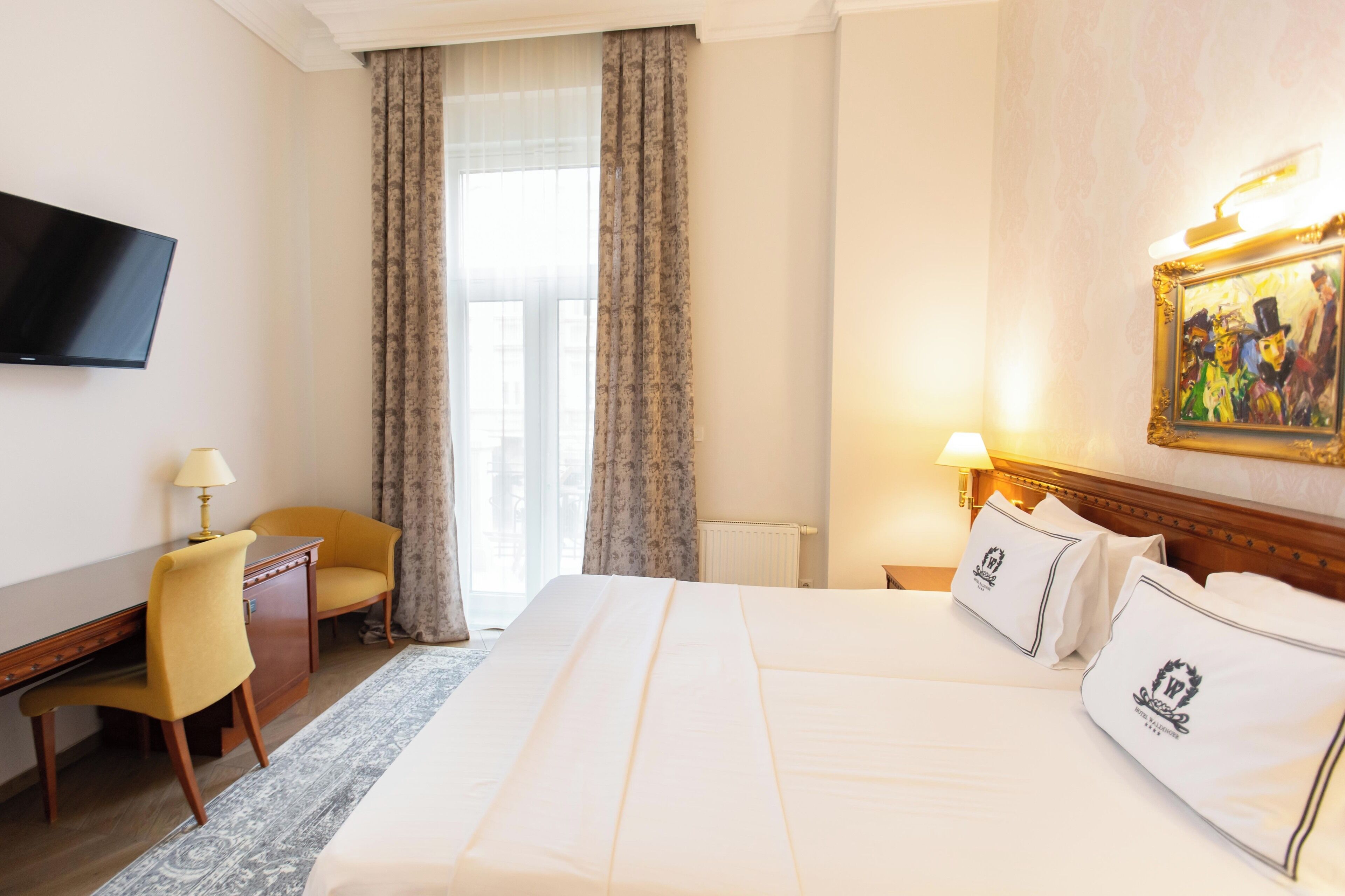 Quarto de hotel com uma cama grande, uma escrivaninha, uma cadeira, uma televisão e um quadro na parede.