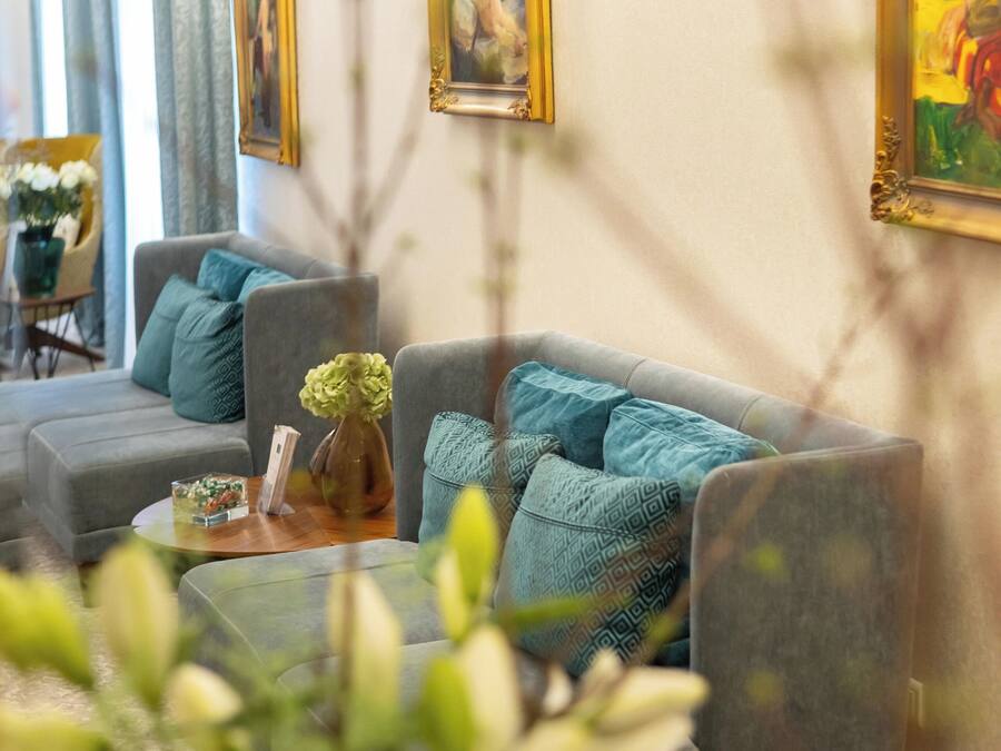 Una sala de estar con un sofá gris, una mesa de centro y un jarrón con flores. En la pared hay cuadros enmarcados y una lámpara sobre la mesa.