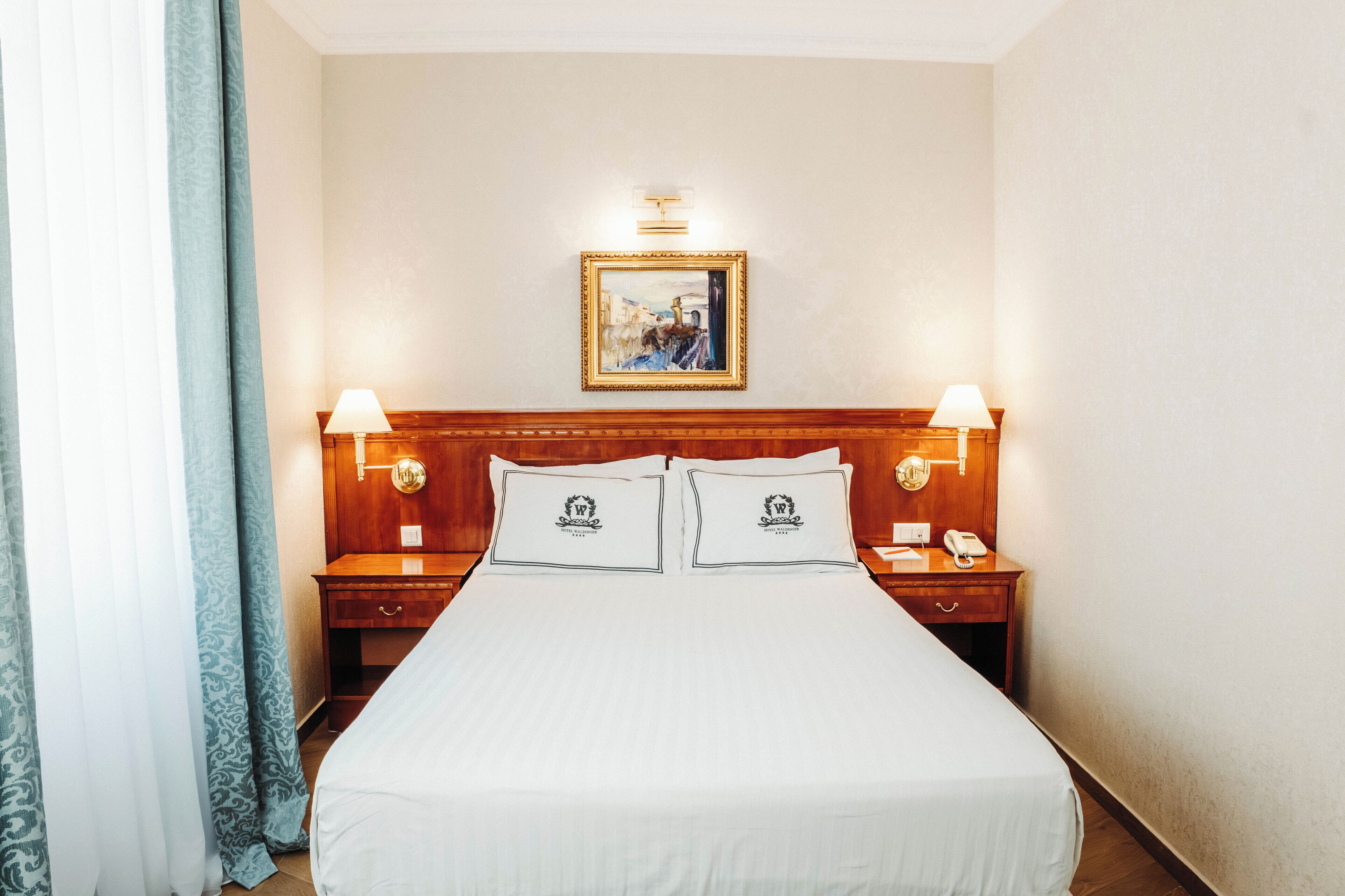 Une chambre d’hôtel avec un grand lit, deux tables de chevet avec des lampes, un tableau encadré au mur et un téléphone sur l’une des tables.