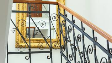 Una escalera con barandillas de hierro negro ornamentadas y un espejo con marco dorado.