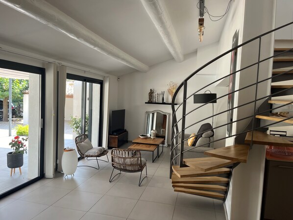 A modern living room with a wooden staircase, a television, and a dining area.