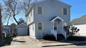 A two-story house with a front porch, a garage, and a small front yard. - Sunshine House - 3BR home close to everything, screen porch! No Linens (Chincoteague)